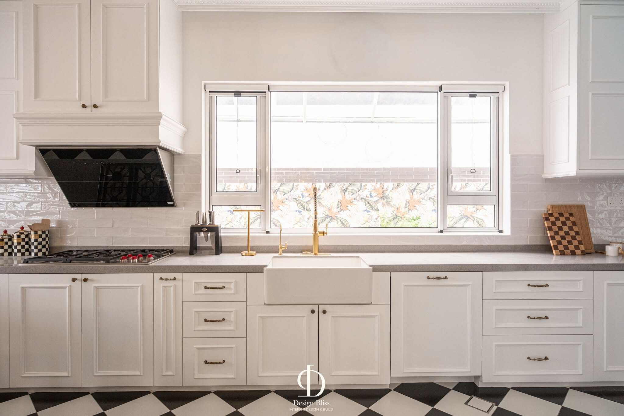 Véra Maison farmhouse sink beneath a large kitchen window with brass faucet